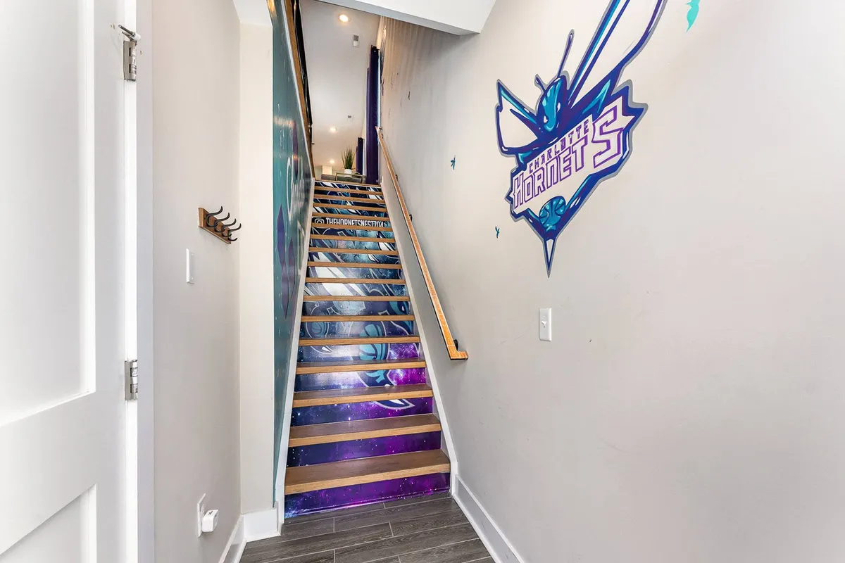 This image showcases a vibrant Hornets mural lining the staircase, complemented by a colorful wall design. The area invites guests to engage with the themed decor as they move through the home, reinforcing the Charlotte sports spirit.