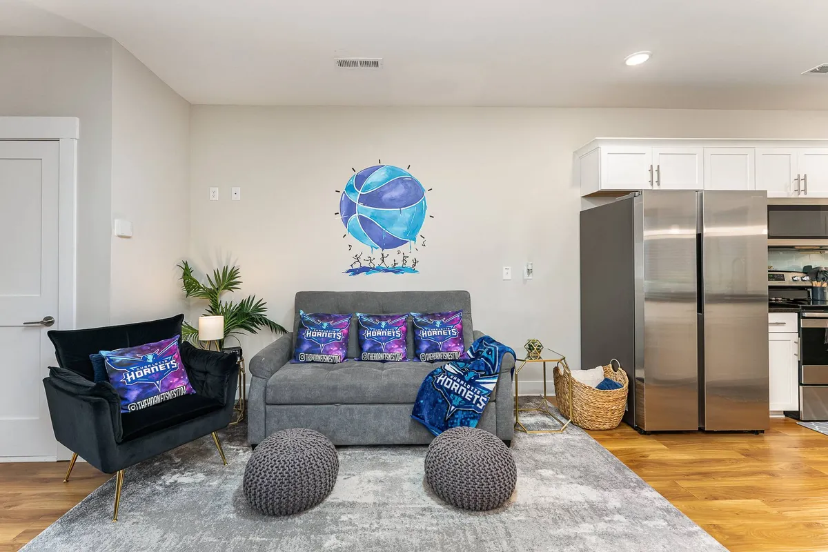 A basketball-themed living space featuring wall art, a comfortable sofa with decorative pillows, throw blankets, and unique seating poufs. The setting is ideal for watching games, entertaining guests, and hosting energetic gatherings.