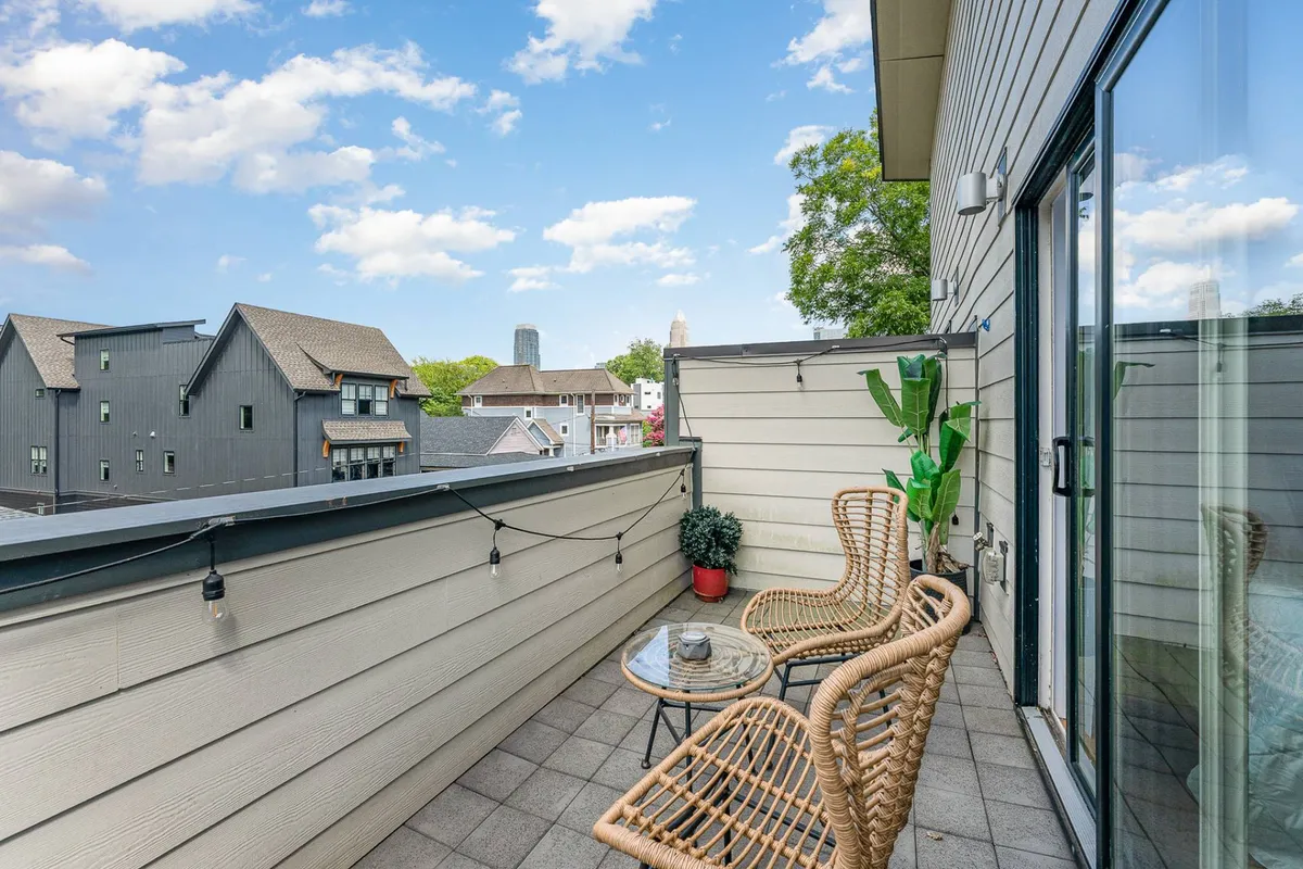 A tranquil private balcony setup with rattan chairs and a glass table, potted greenery, and expansive city views. The scene is set for morning coffee or evening relaxation, with the city skyline providing a stunning backdrop.