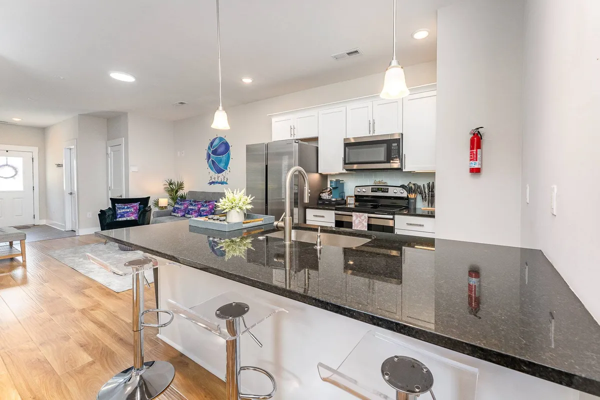 A welcoming kitchen and dining area featuring a kitchen island with bar stools, stainless steel appliances, and decorative wall art. The open-concept design connects seamlessly to the living area, visually supporting the narrative of conversations flowing from kitchen to dining to living.