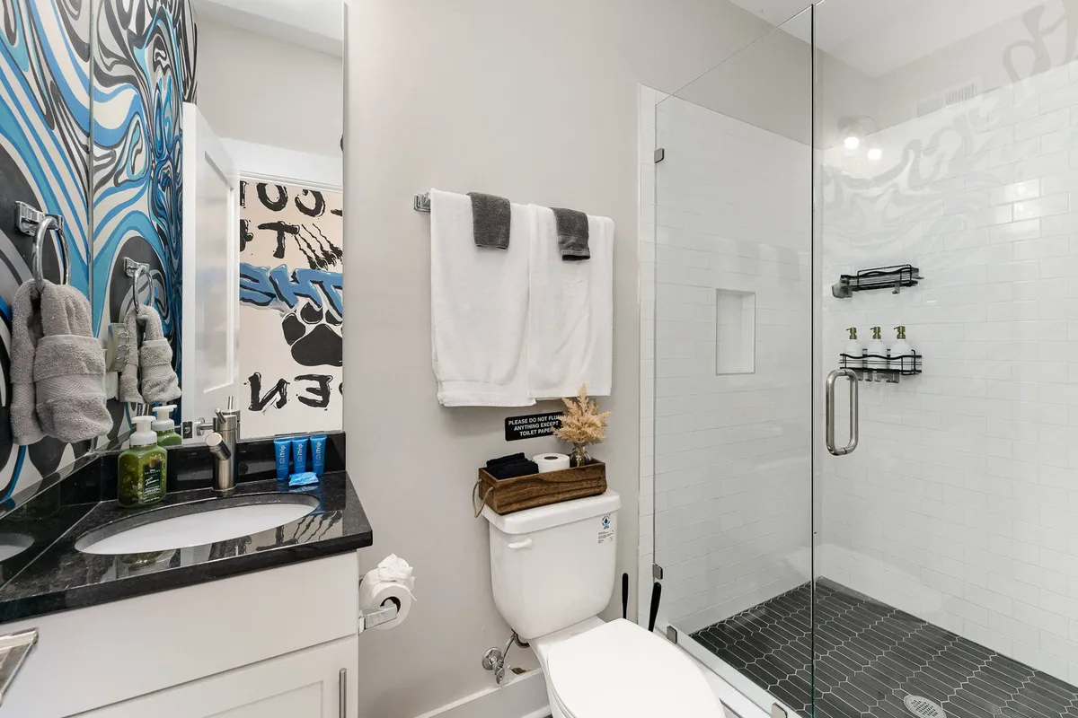 A modern, spa-like bathroom featuring colorful wall art, a sleek vanity, and a spacious glass shower enclosure. Soft lighting and clean lines create an inviting environment ideal for relaxation and personal care.