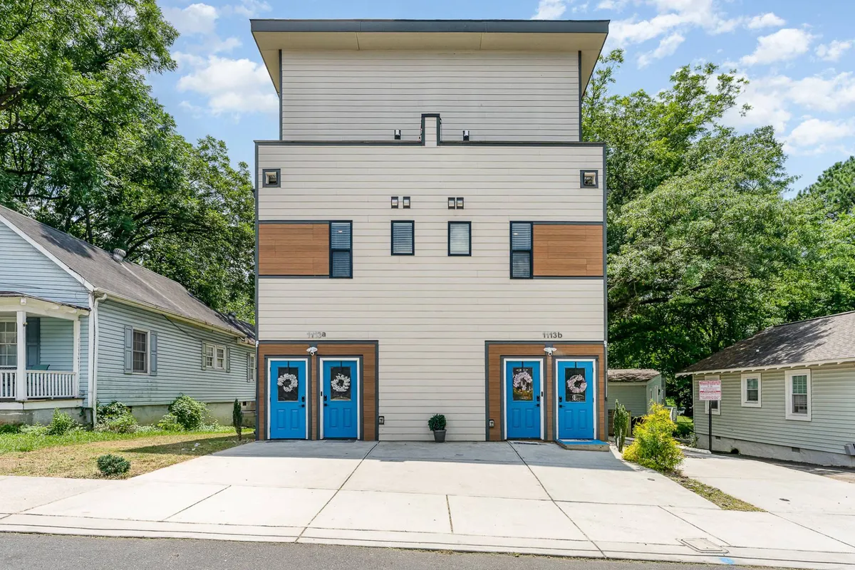 This exterior image features distinctive blue doors set in modern architecture, accompanied by surrounding greenery. The dual front entrances are visible, visually representing the duplex's multiple entry points.
