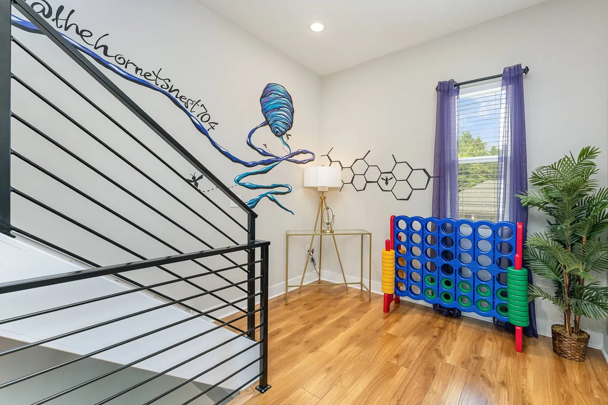 A playful interior spotlights a colorful Connect Four game, an artistic wall mural, and a staircase, with cozy lighting inviting guests to gather and play. The setting is creative and social, ideal for group interactions.