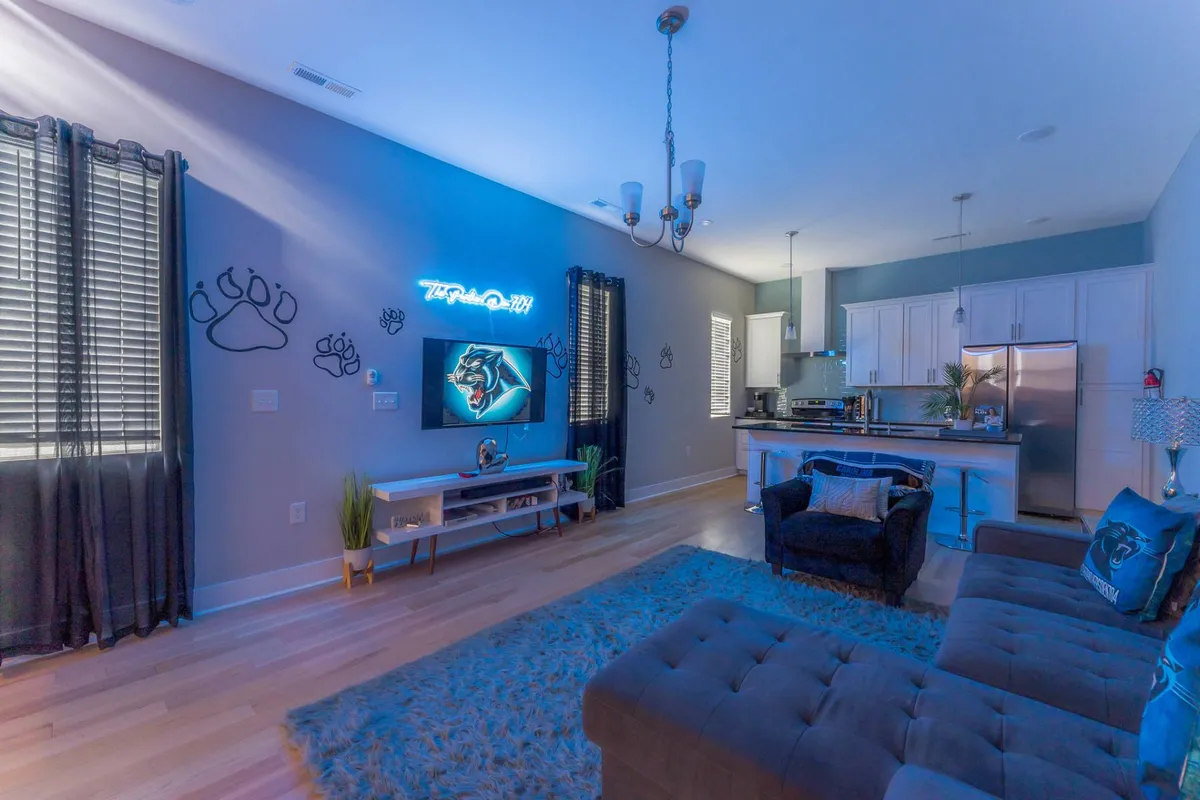 A playful and relaxed lounge area featuring a neon sign, panther-themed artwork, a comfortable sofa, and a cozy rug. It’s a vibrant, themed space ideal for smaller groups or fans looking for a unique stay.