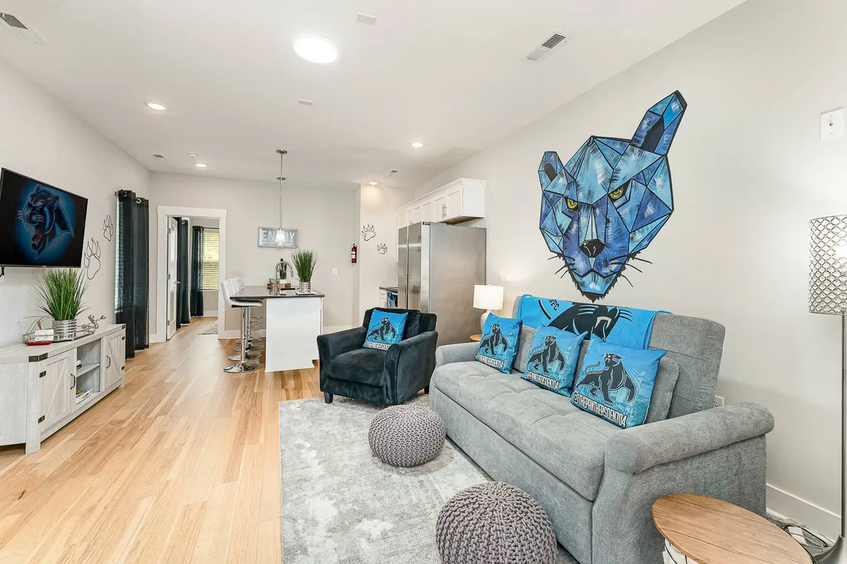 A stylish living space featuring a geometric wolf mural, a plush sofa, a modern kitchen island, and an entertainment unit with a large TV. The setup is inviting for casual conversations, pre-dinner gatherings, or relaxing after a night out.