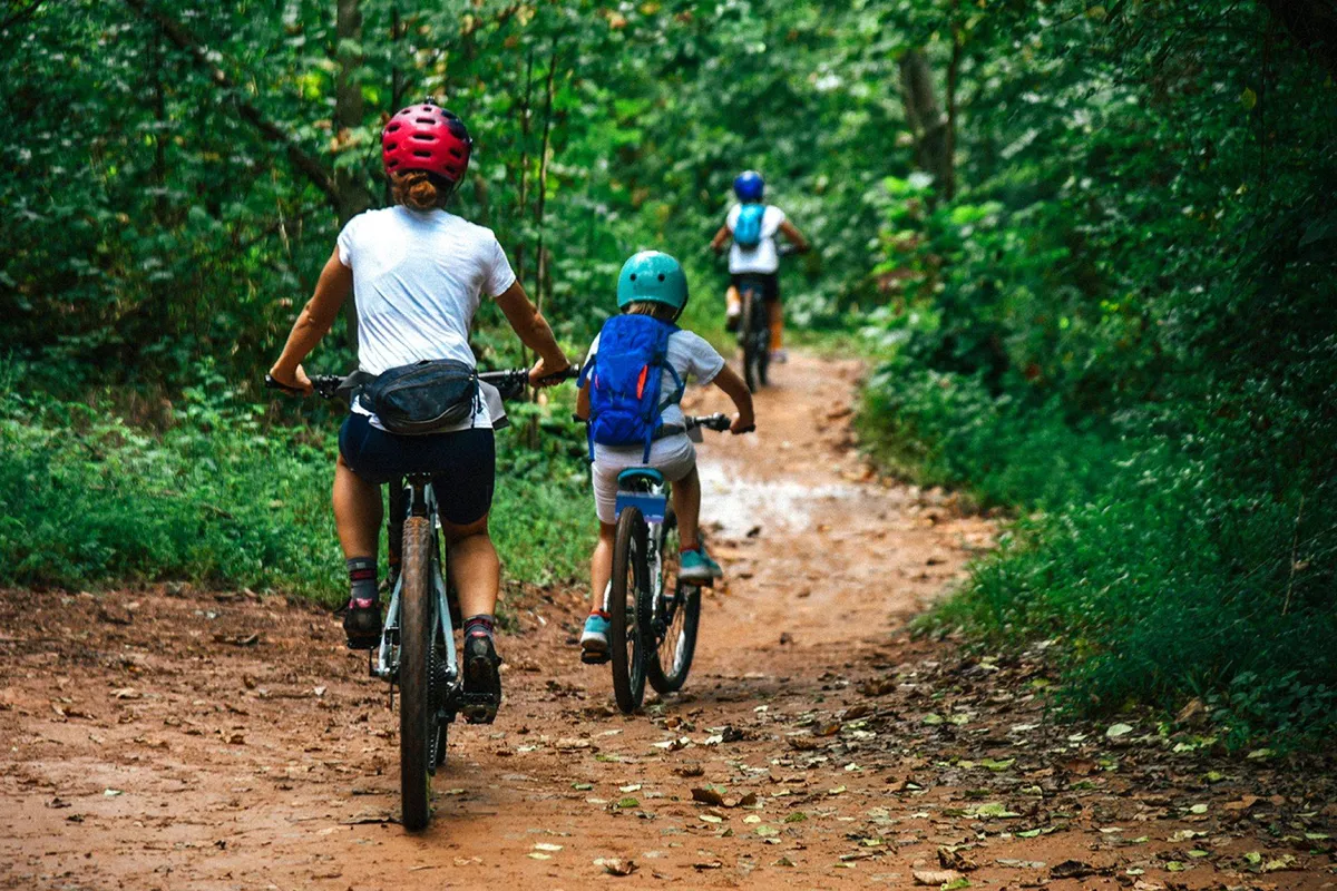 This exterior image features cyclists enjoying a winding pathway flanked by lush trees, capturing a vibrant moment of outdoor activity. The scene conveys a sense of community, adventure, and family bonding amidst nature, with the green environment echoing the park and trail setting described in the section.