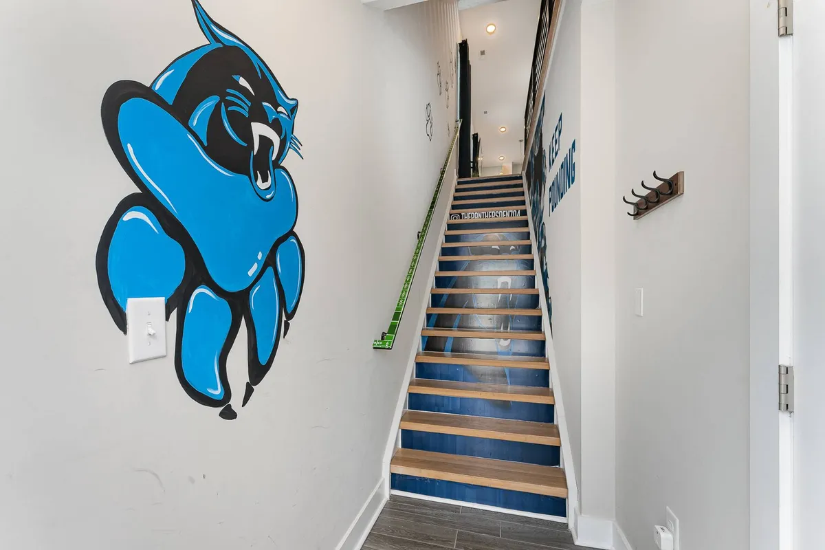 This image features a striking blue panther mural prominently displayed near the staircase, with wall hooks and a playful atmosphere. The mural makes a powerful first impression, immediately establishing the sports and local team theme as soon as guests enter the property.
