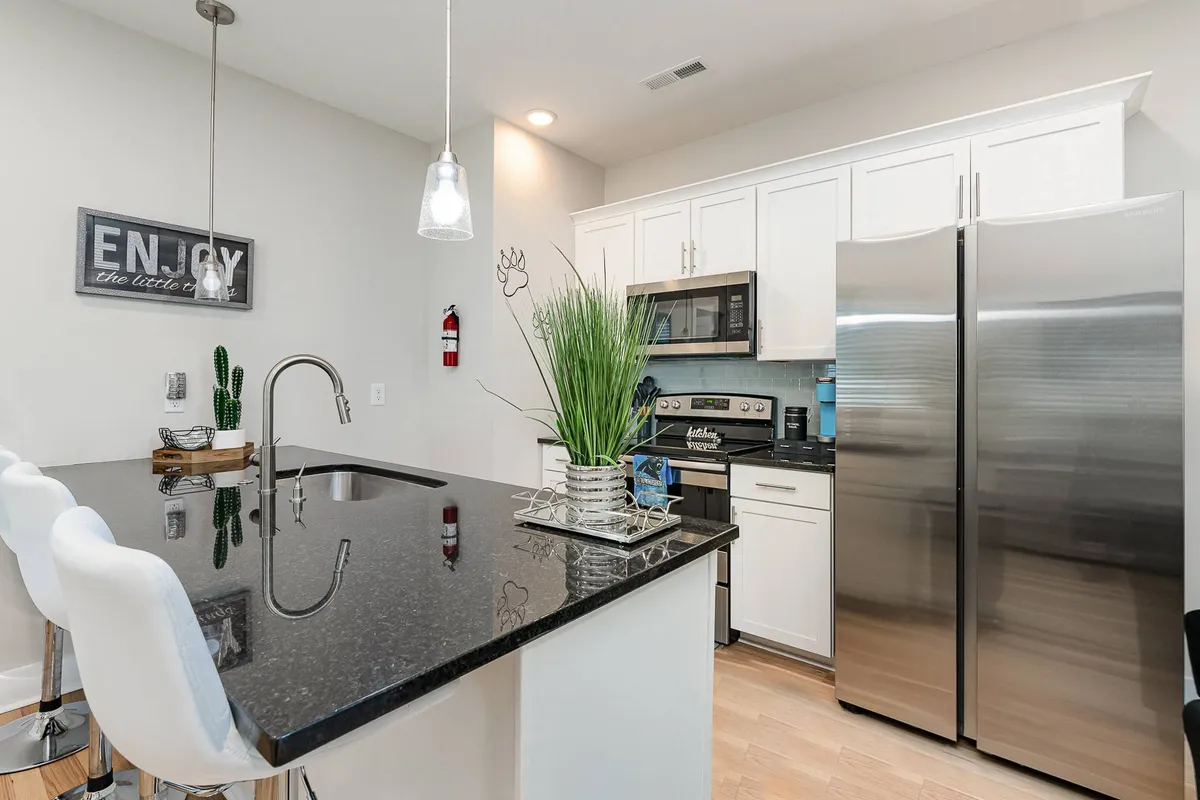 A bright, open-concept kitchen featuring a large kitchen island, stainless steel appliances, a decorative plant, and framed artwork on the wall. The island offers space for prepping and casual dining, while the contemporary finishes give the space a modern, welcoming vibe.